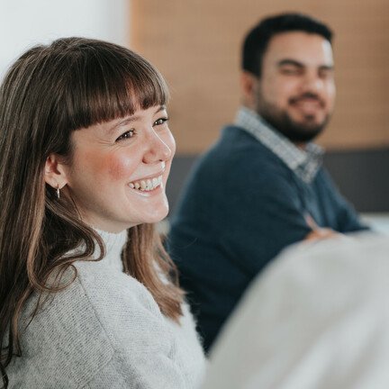Zwei Personen sind zu sehen. Eine Frau lachende mit dunklen Haaren steht im Fokus.